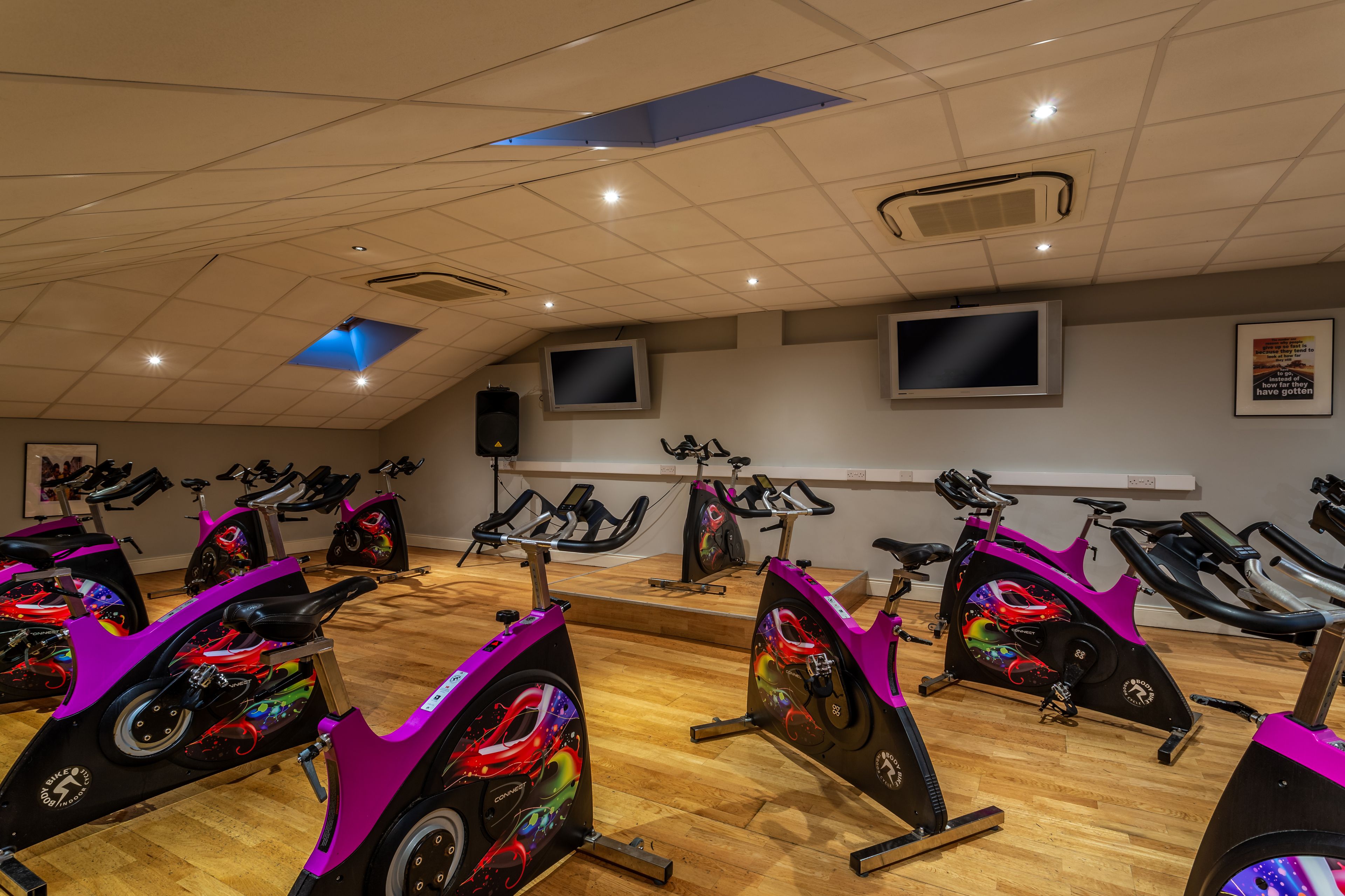 A fitness studio with stationary bikes, a TV, and a motivational poster on the wall.