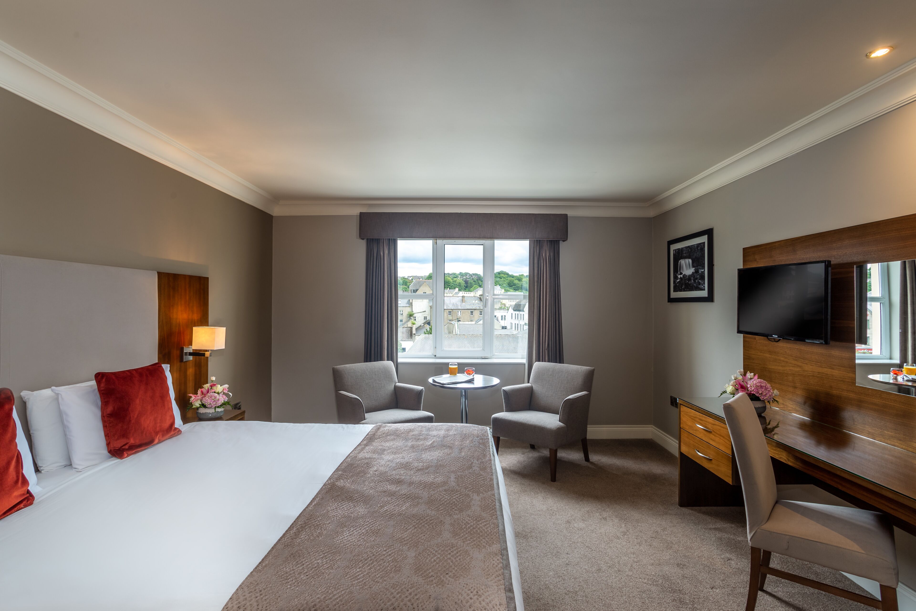 Habitación de hotel con una cama, dos sillones, un escritorio, un televisor y una ventana con vista a edificios.