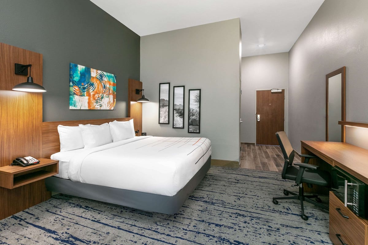 A hotel room with a large bed, a desk, a chair, a phone, and artwork on the walls.
