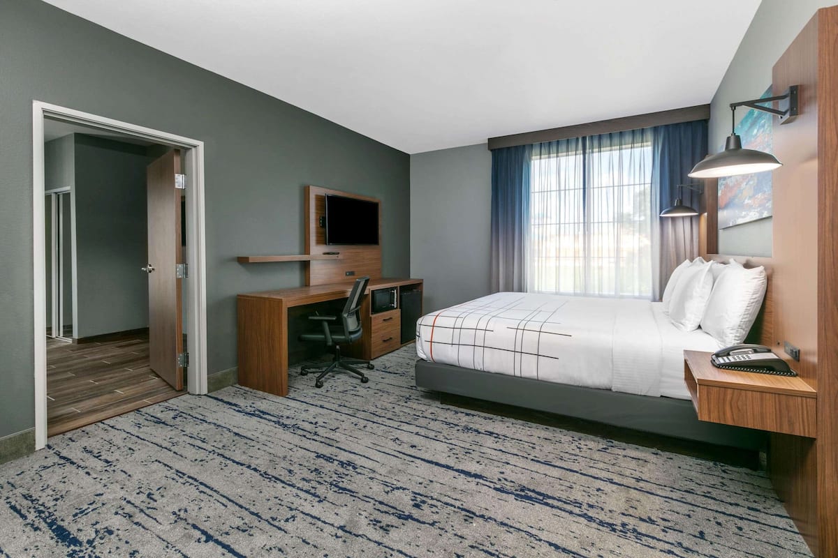 A hotel room with a bed, desk, chair, TV, and a door leading to another room.