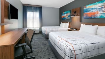 A hotel room with a desk, two beds, a TV, and artwork on the walls.