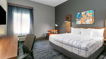 A hotel room with a large bed, a desk, a chair, a lamp, and a painting on the wall.