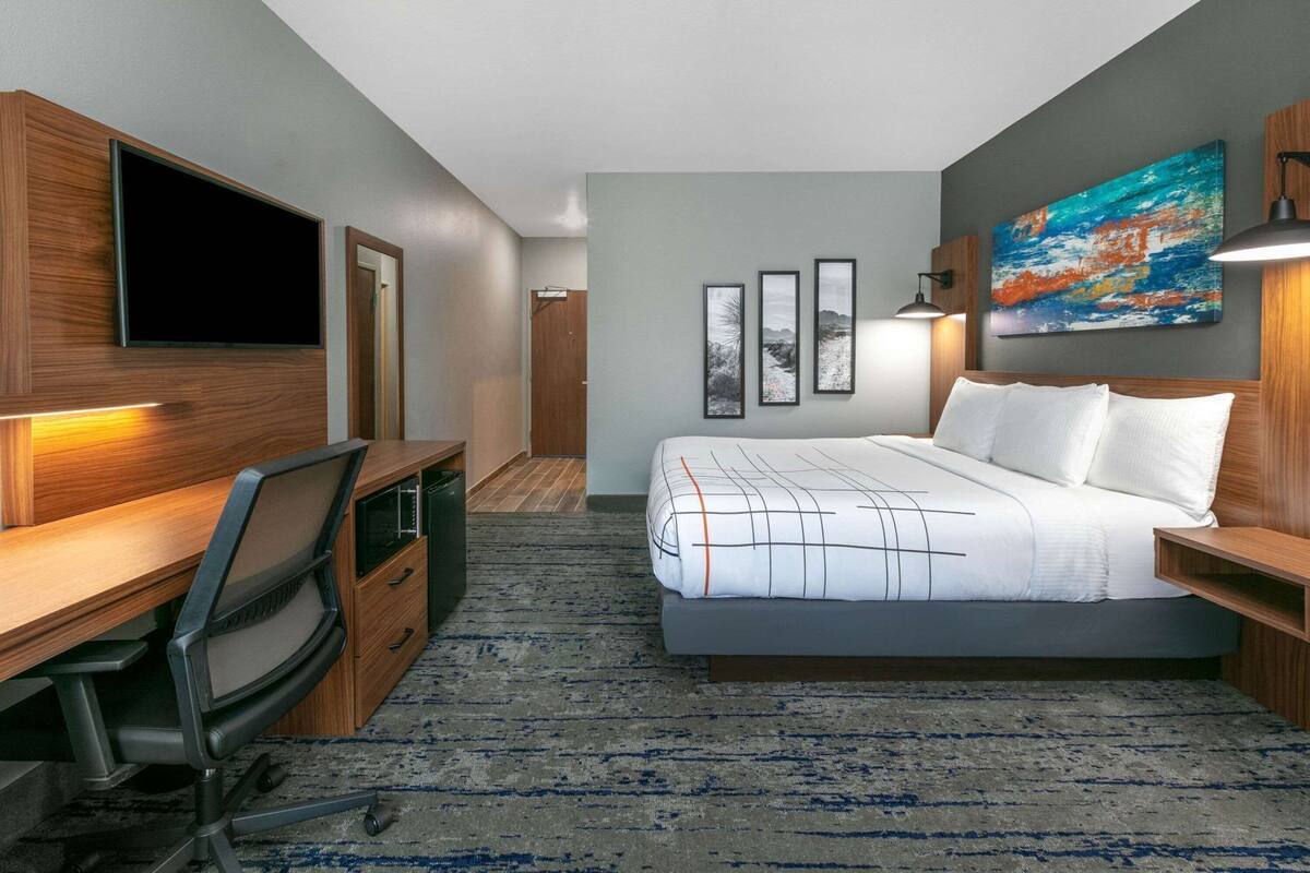 A hotel room with a bed, desk, chair, TV, artwork, and framed pictures.