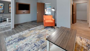 Une chambre d’hôtel moderne avec un téléviseur à écran plat fixé au mur, un fauteuil orange, une table en bois et un tapis coloré.