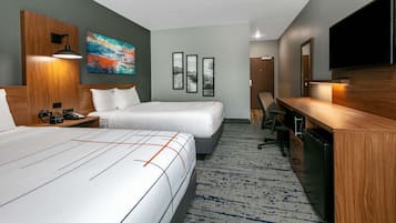 Quarto de hotel com duas camas, uma escrivaninha, televisão e obras de arte nas paredes.