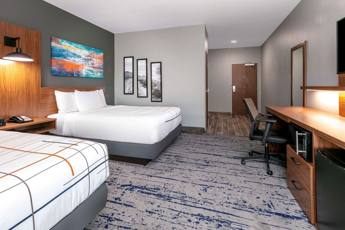 A hotel room with a bed, bedside table, lamp, desk, chair, and a large mirror.