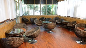 Een café met rieten stoelen en tafels, bakstenen muren en grote ramen.