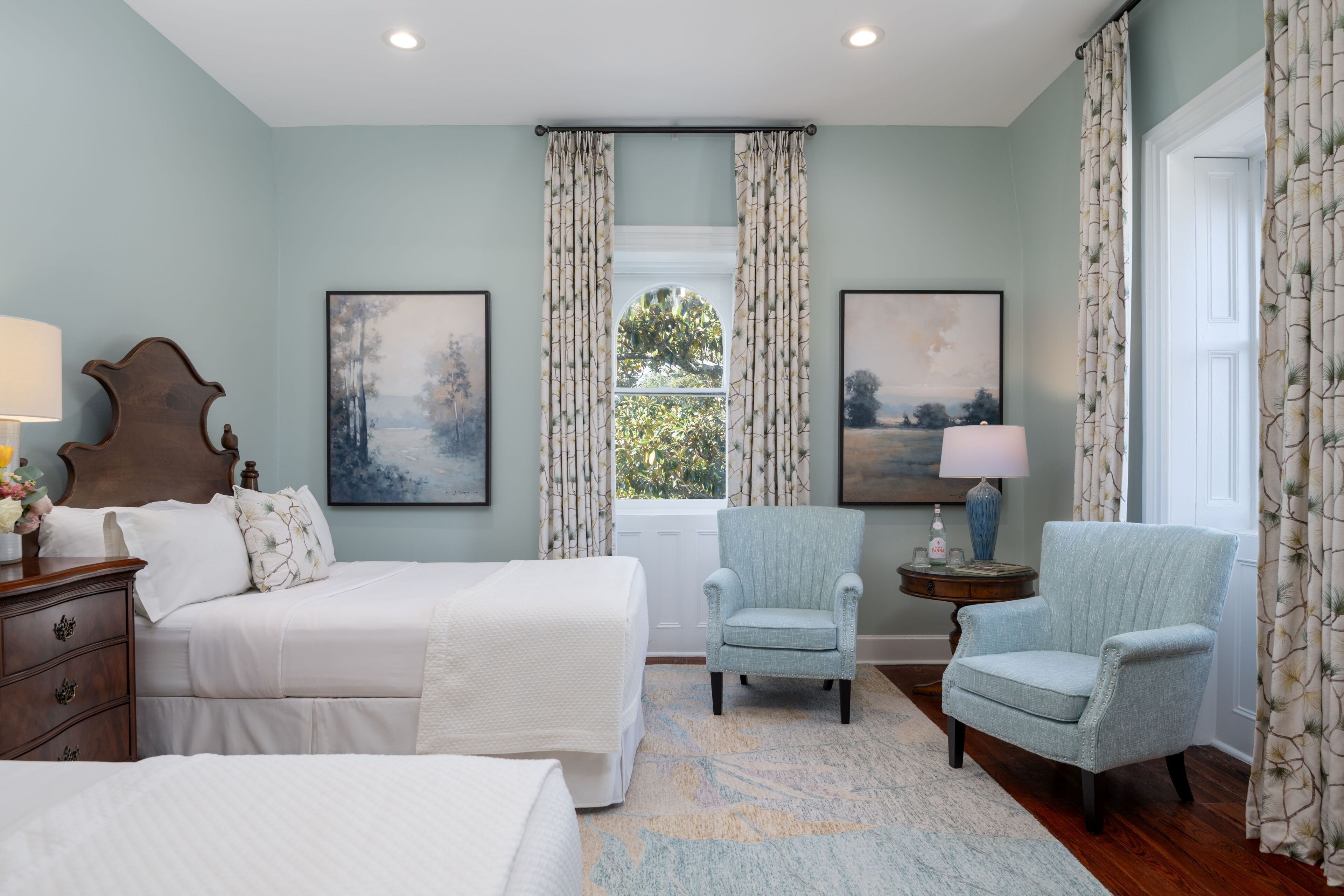 A bedroom with a large bed, two armchairs, a nightstand, and a window with curtains.