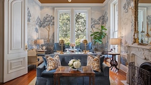 A luxurious living room with a grand chandelier, a fireplace, and a large window with a view of trees.
