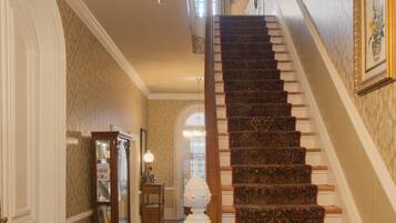 A grand staircase with a patterned carpet, a chandelier, and a wooden floor.