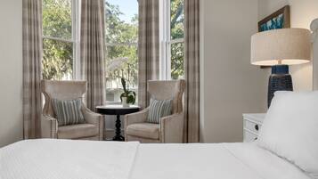 Une chambre d’hôtel avec un grand lit, deux fauteuils, une petite table avec une plante et une table de chevet avec une lampe.
