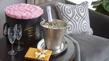 A black bucket with pink roses, a champagne bottle in a silver bucket, two empty champagne flutes, and a small gift box on a round table.