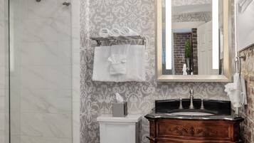 A bathroom with a glass shower enclosure, a white toilet, a vanity with a mirror, and patterned wallpaper.