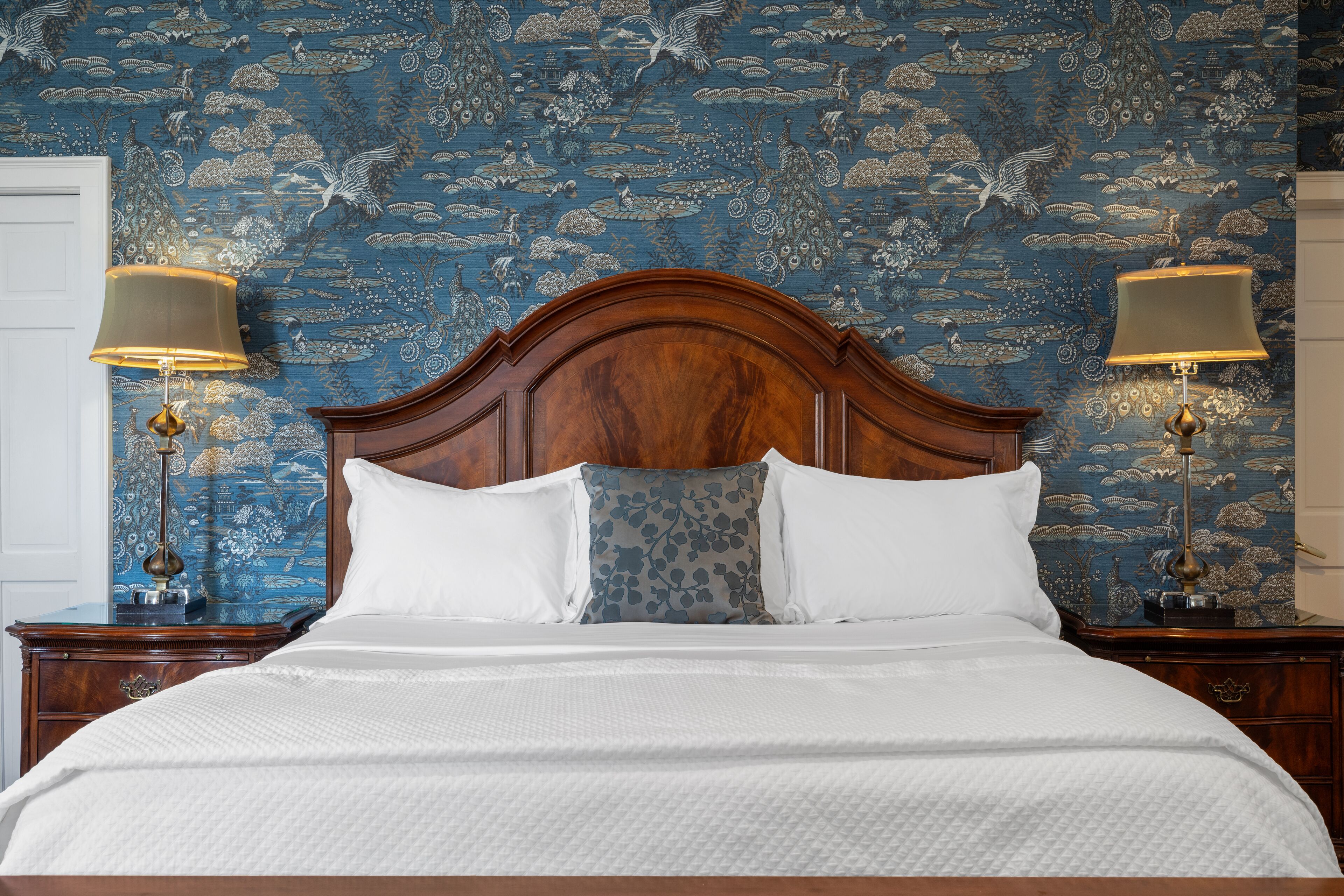 A neatly made bed with white linens, a wooden headboard, and two bedside lamps.