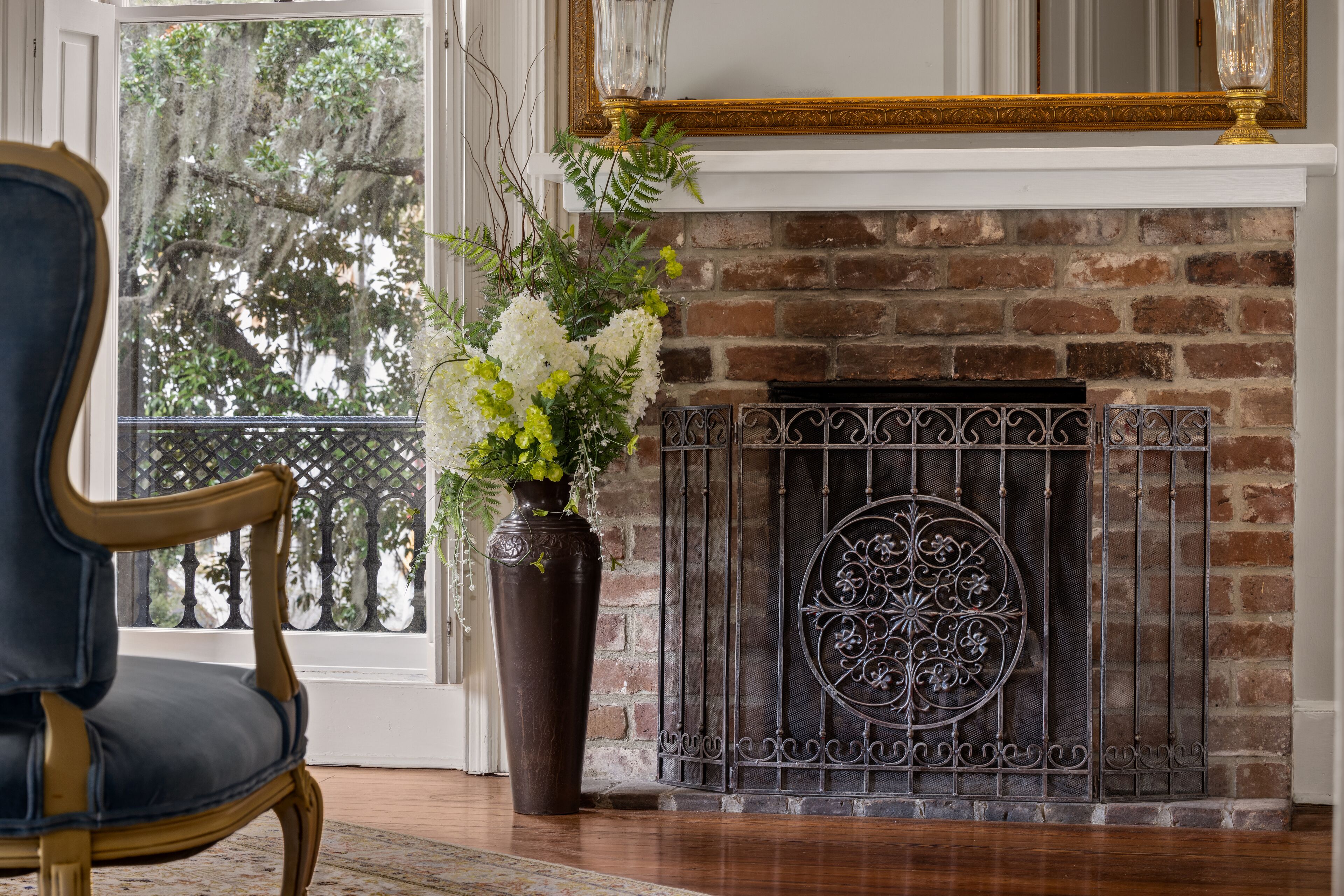A room with a brick fireplace, a large vase with flowers, and a classic chair.
