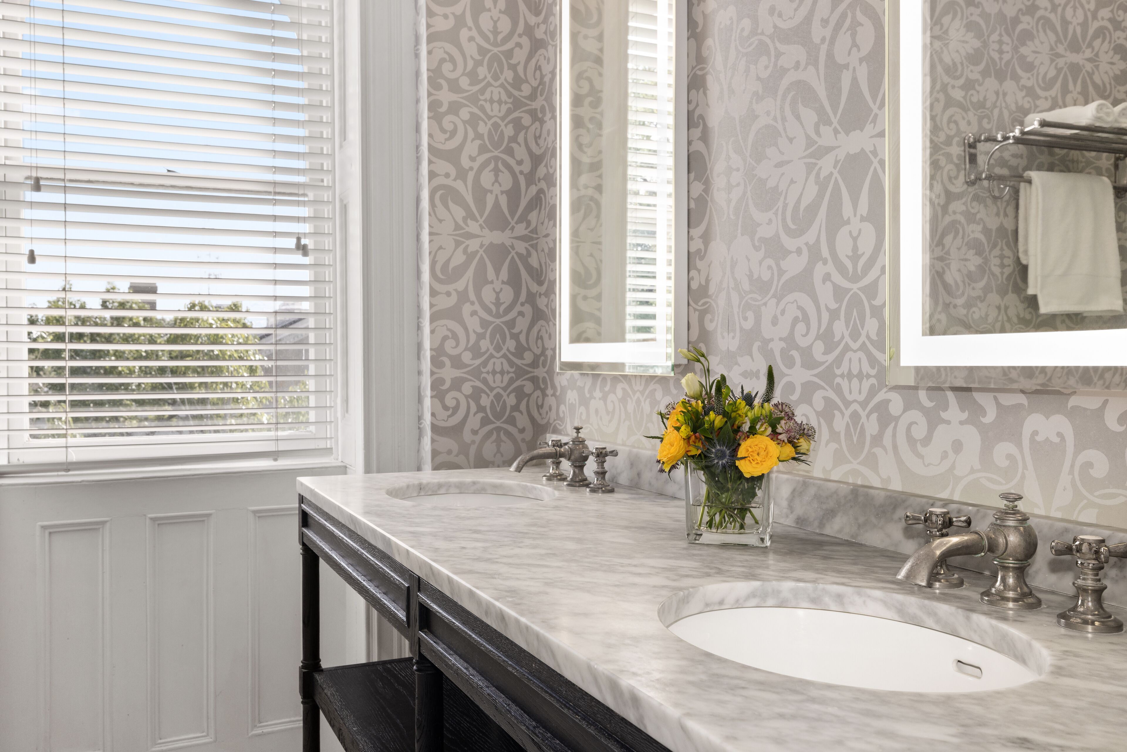 A bathroom with two sinks, a mirror, and a window with blinds.
