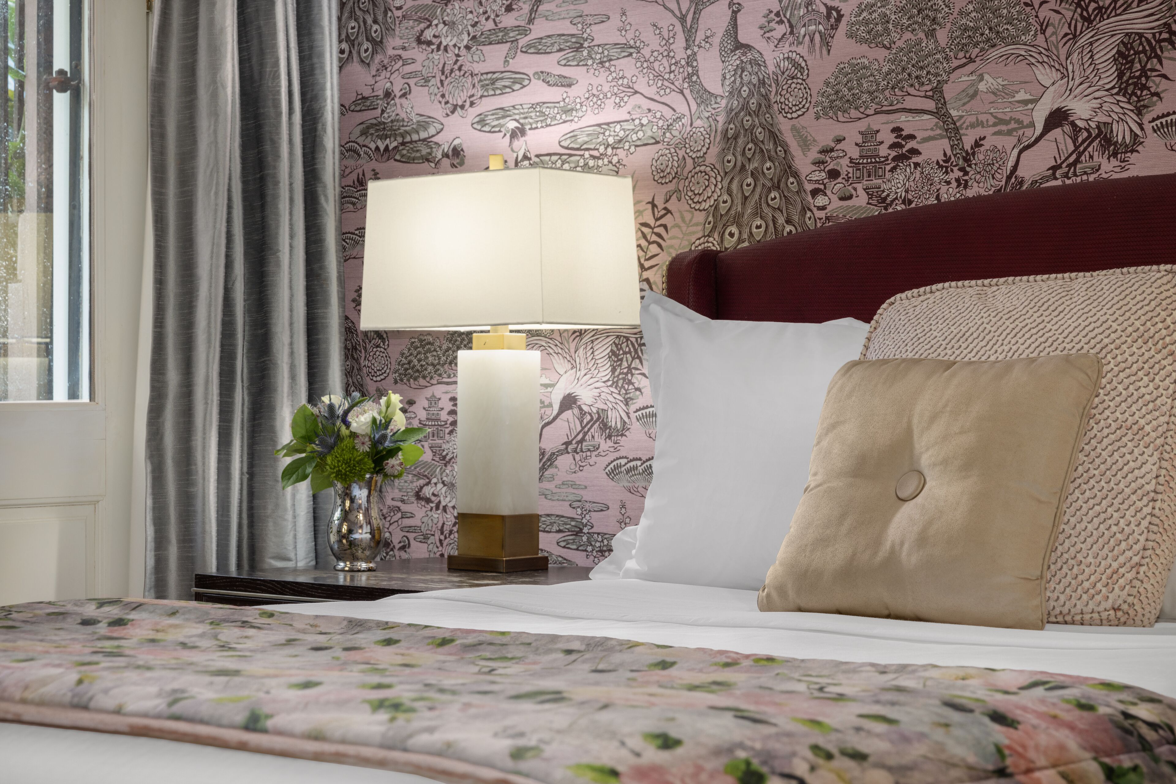 A neatly made bed with a floral bedspread, a bedside lamp, and a decorative vase with flowers.