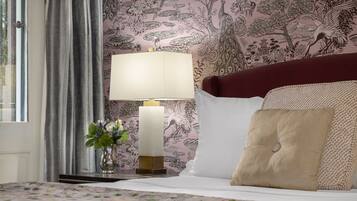 A neatly made bed with a floral bedspread, a bedside lamp, and a decorative vase with flowers.