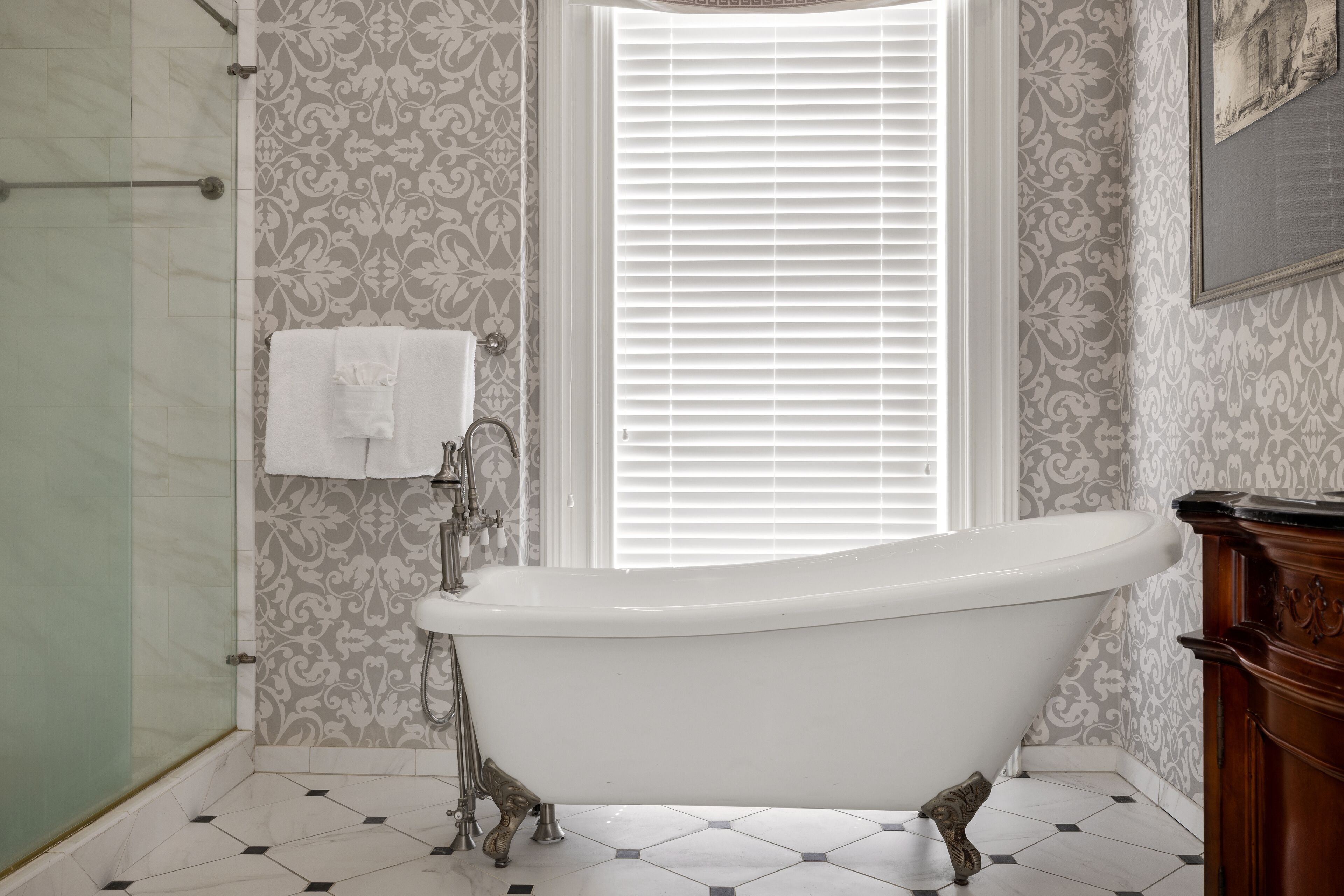 A bathroom with a freestanding bathtub, a shower, and patterned wallpaper.