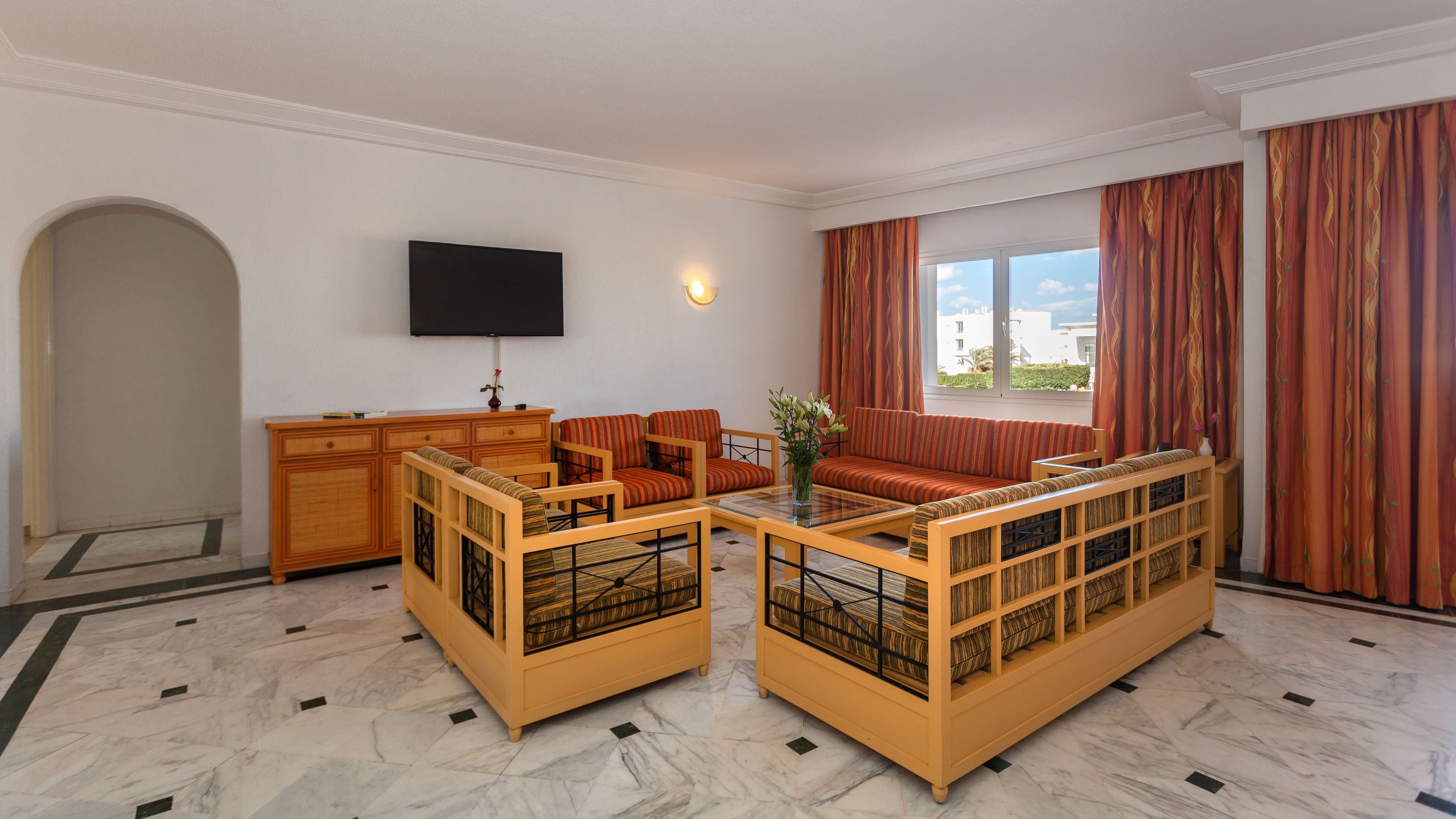 Une chambre d’hôtel équipée d’un canapé, d’une télévision, d’un bureau et d’une fenêtre avec des rideaux.
