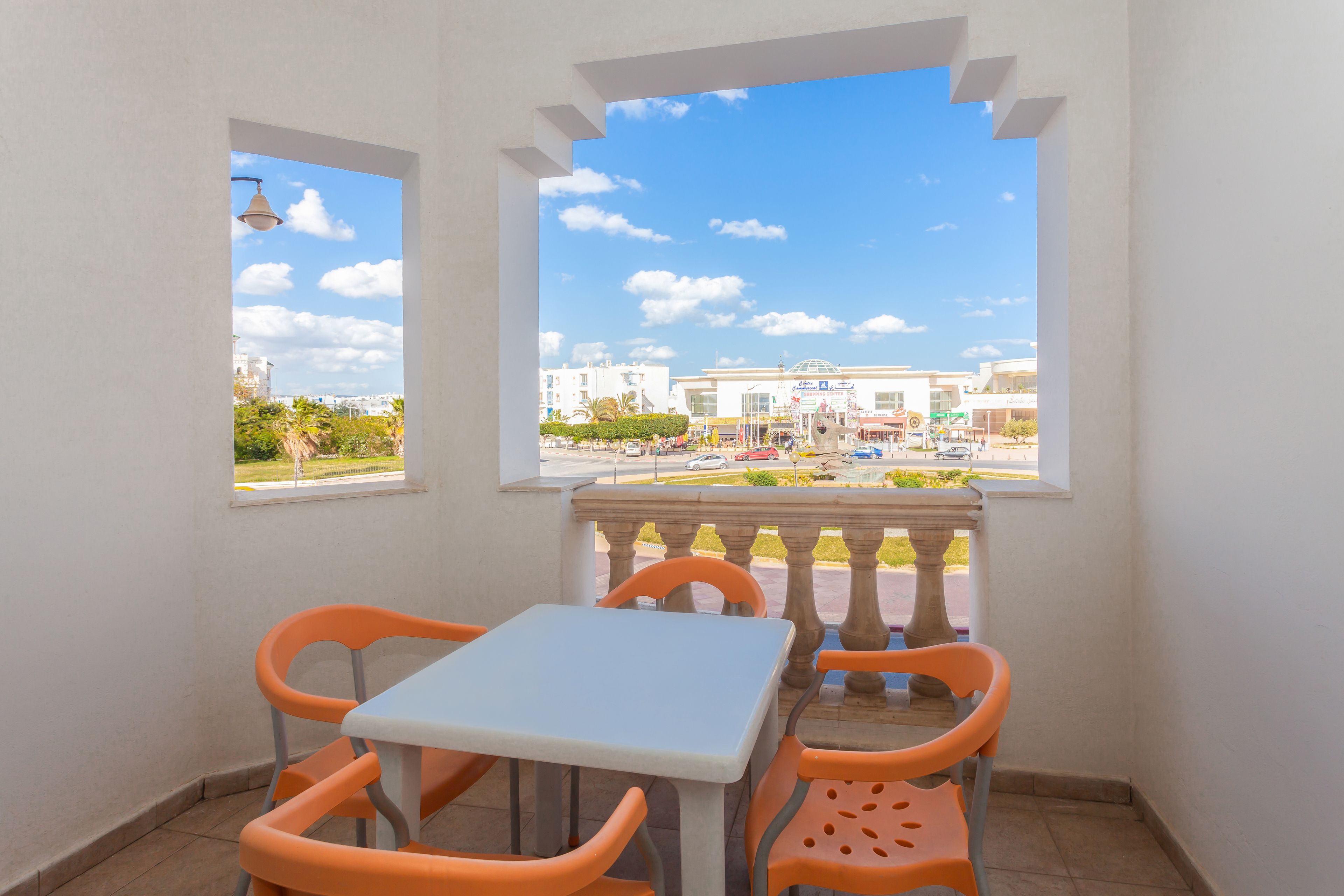A balcony with a table and chairs, overlooking a street with buildings and a clear sky.