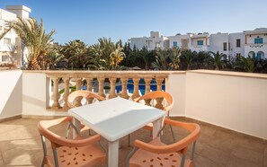 A terrace with a white table and orange chairs, overlooking a pool and palm trees. - Corail Apart’hotel & Splash park (Hammamet)
