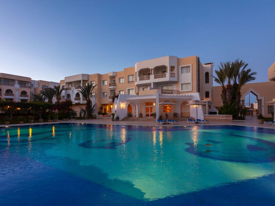 A hotel with a swimming pool, multiple balconies, and palm trees.