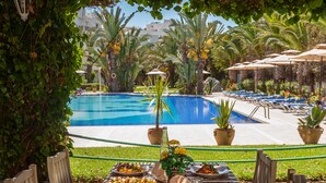 An outdoor dining area with a pool view, wooden chairs, and a table set with food.