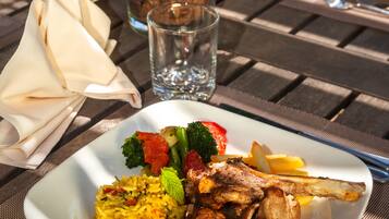 A square plate of food with meat, vegetables, and rice, placed on a wooden table with a napkin and a glass of water.