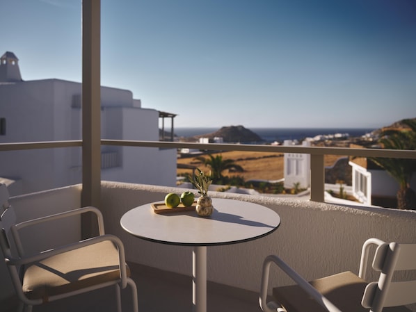 A balcony with a round table, two chairs, and a view of the coastline.