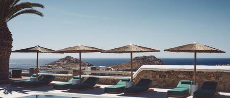 A poolside area with lounge chairs and umbrellas, overlooking a body of water and a rocky landscape.