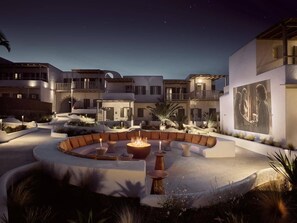 A courtyard with a circular seating area, a fire pit, and a large wall with a poster. - NUMO Mykonos Boutique Resort (Mykonos)