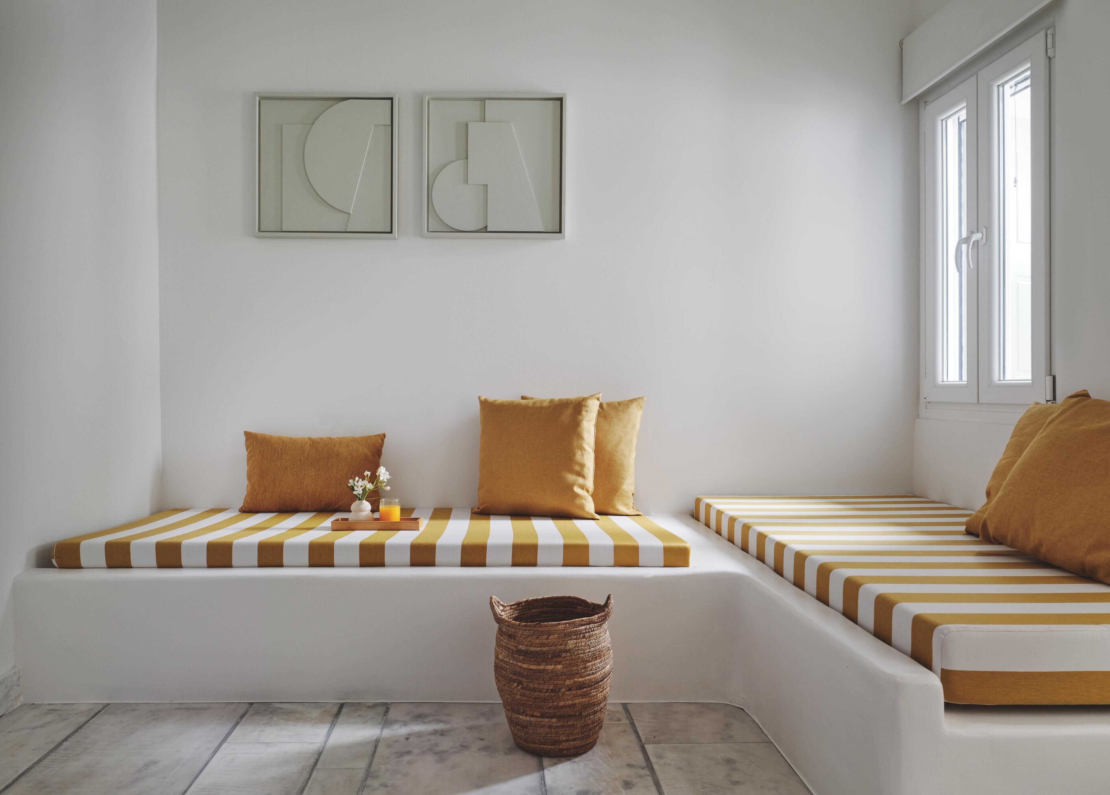 A minimalist room with a white and yellow striped sofa, a small woven basket, and two abstract wall art pieces.