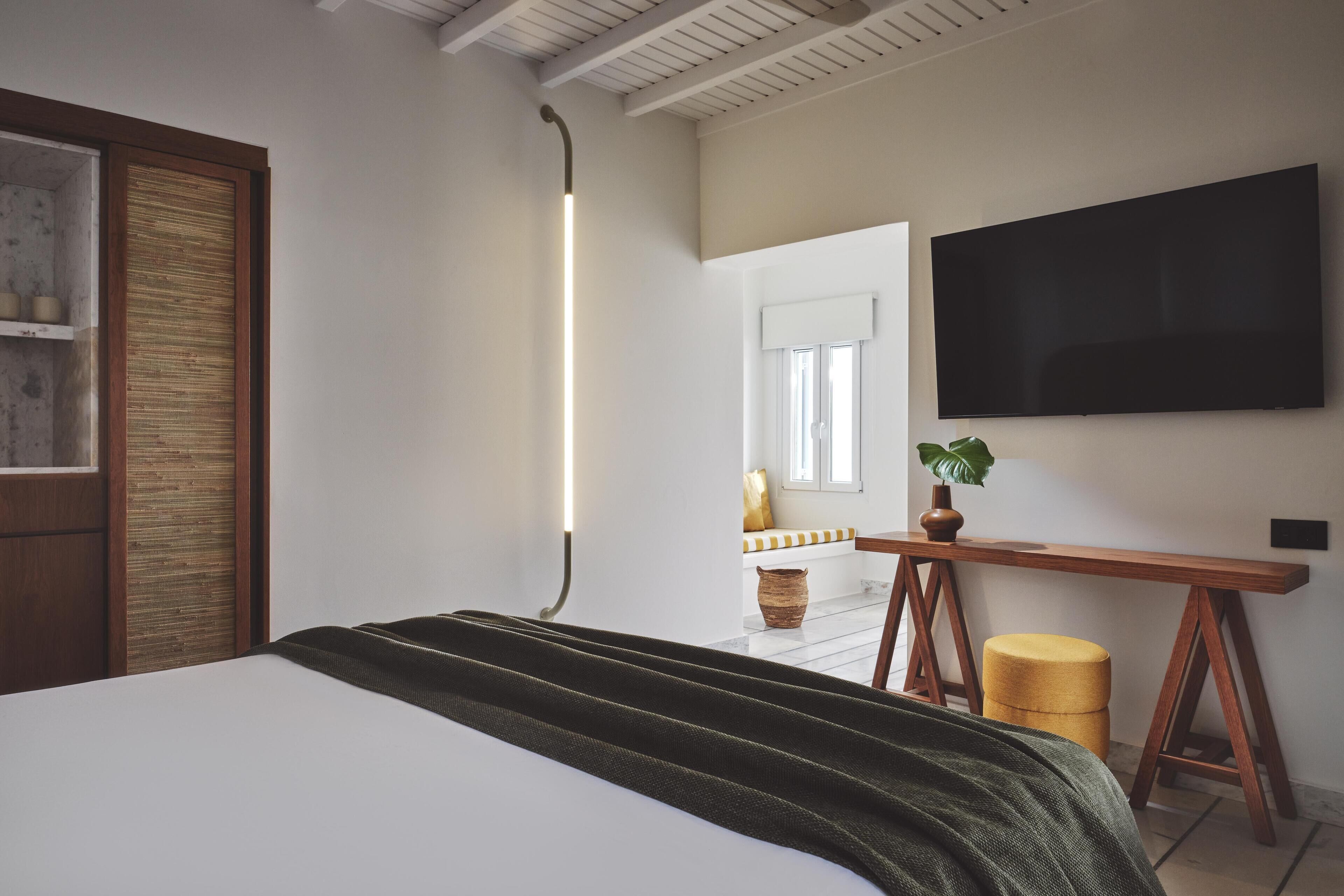 A modern bedroom with a large bed, a wooden desk, a television, and a window with a view of the outside.