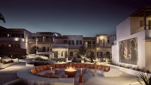 A well-lit outdoor seating area with a circular arrangement of sofas and tables, surrounded by a landscaped garden with palm trees and shrubs.