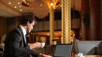 A man in a suit using a laptop in a well-lit, elegantly decorated room with a sofa and a table with a teapot.