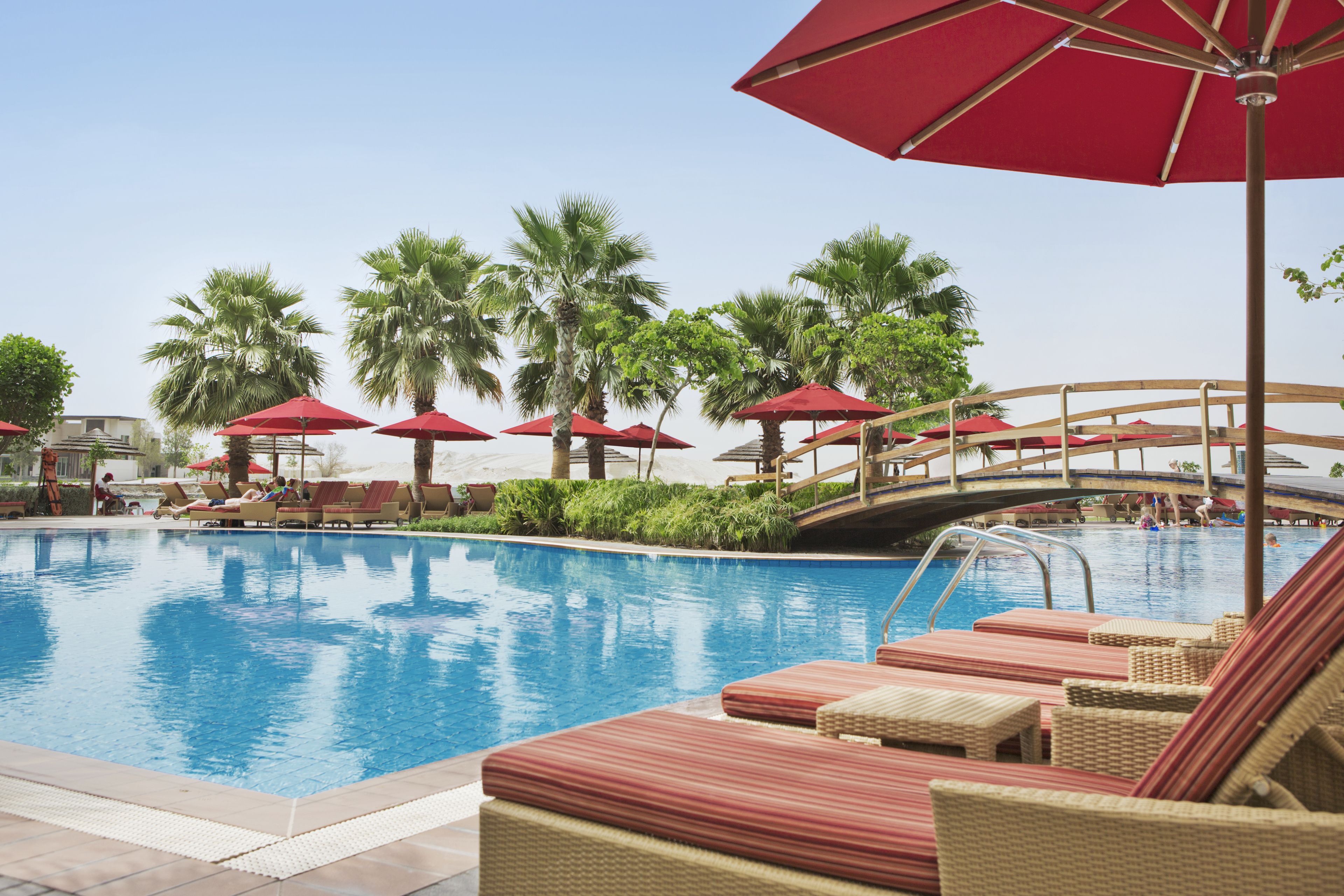 A pool area with lounge chairs and red umbrellas, surrounded by palm trees.
