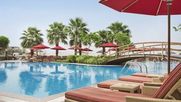 A pool area with lounge chairs and red umbrellas, surrounded by palm trees.