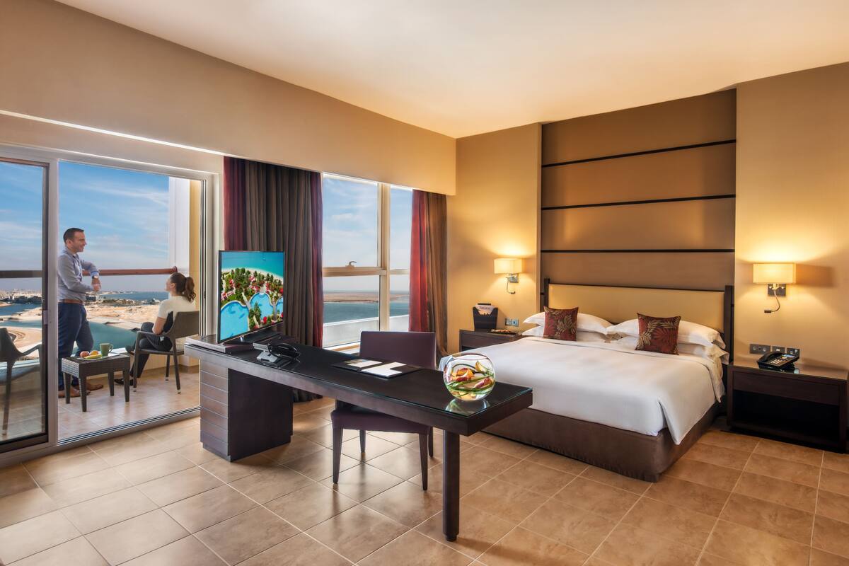 A hotel room with a bed, desk, and a view of the beach.