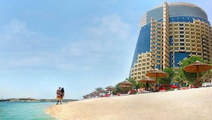 A beachside hotel with a large blue and beige building, sun umbrellas, and a sandy beach. - Khalidiya Palace Rayhaan by Rotana (Abu Dhabi)