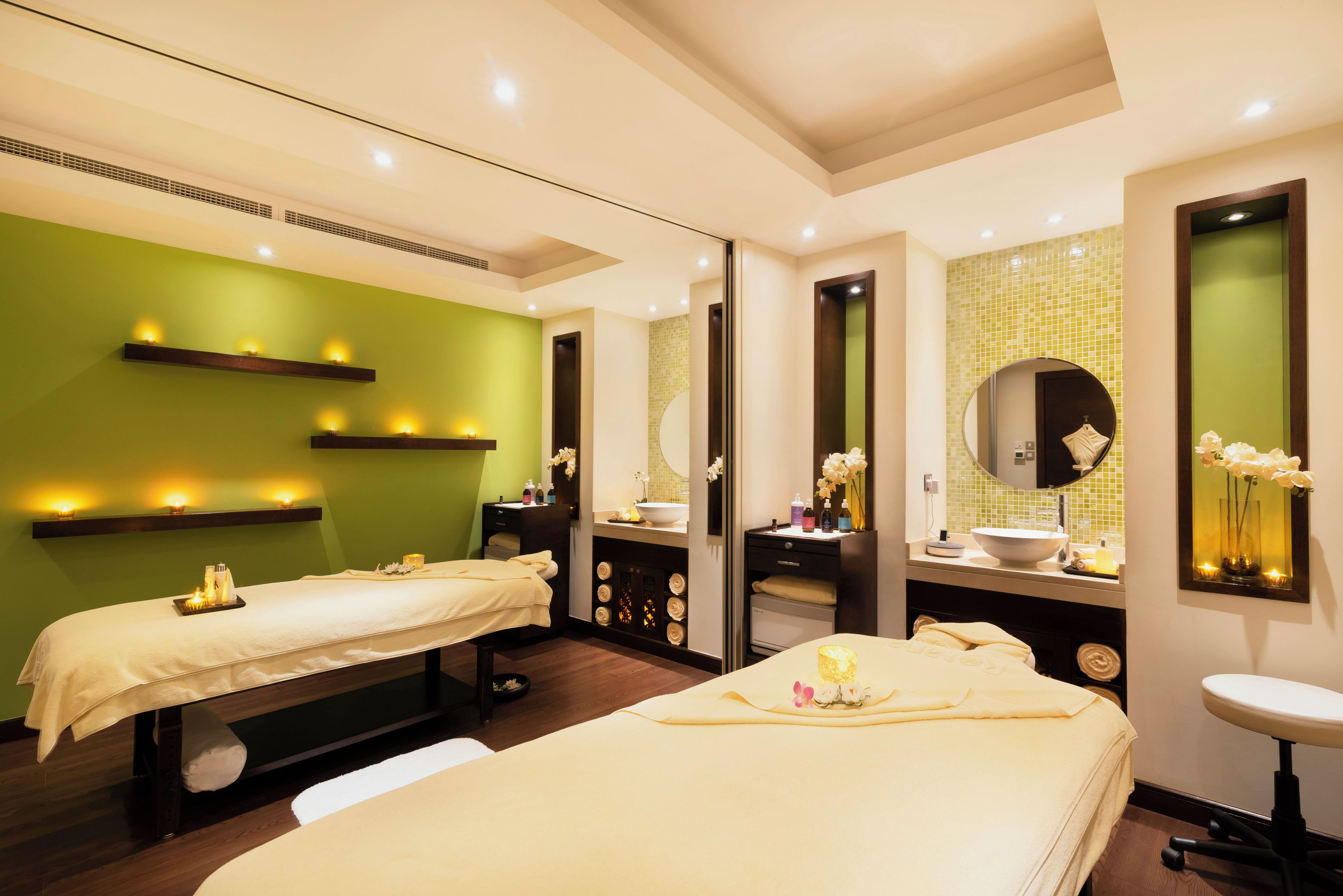 A spa room with two massage tables, a large mirror, and a vanity with a sink.