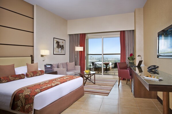 Una habitación de hotel con una cama grande, un escritorio, un sofá, una mesa de comedor y un balcón con vistas.