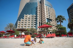Una playa con sombrillas rojas, sillas de descanso y un edificio moderno al fondo.