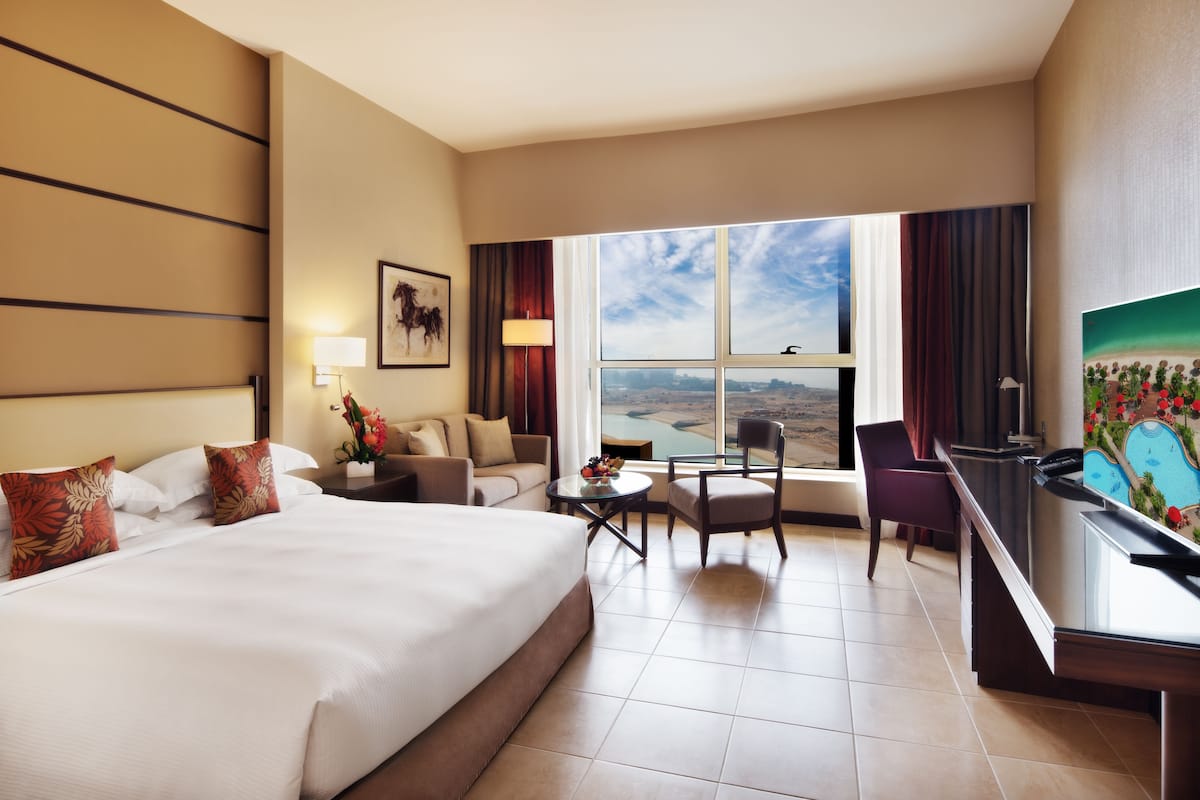 A hotel room with a large bed, a desk, a chair, a small table, and a view of the outdoors.