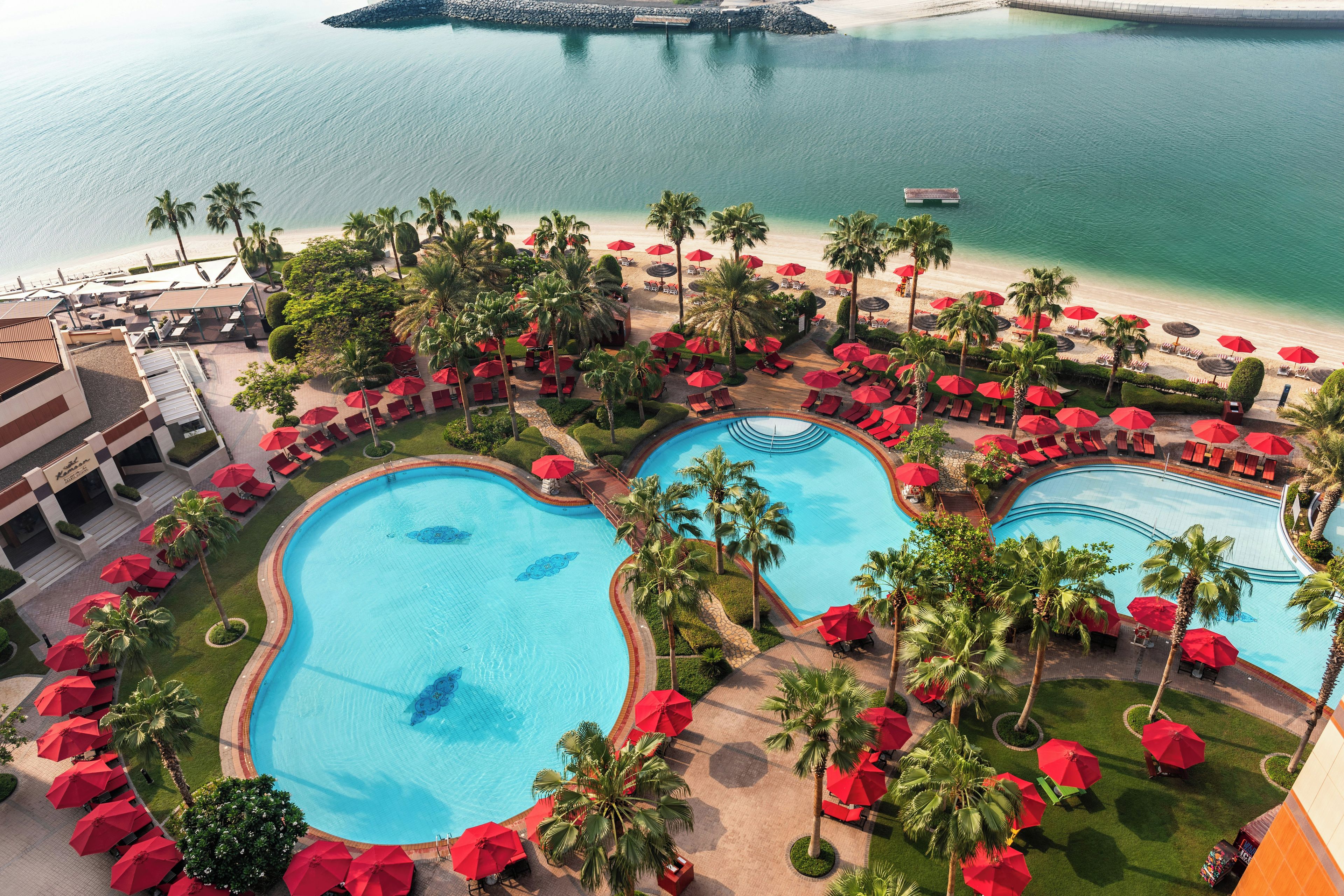 A resort with multiple swimming pools, a beach, and red umbrellas.