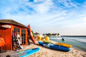 A beachside building with ski equipment and kayaks, a thatched roof, and a view of the sea. - Khalidiya Palace Rayhaan by Rotana (Abu Dhabi)