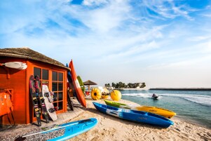 Um edifício à beira-mar com equipamentos de esqui e caiaques, um telhado de palha e vista para o mar.