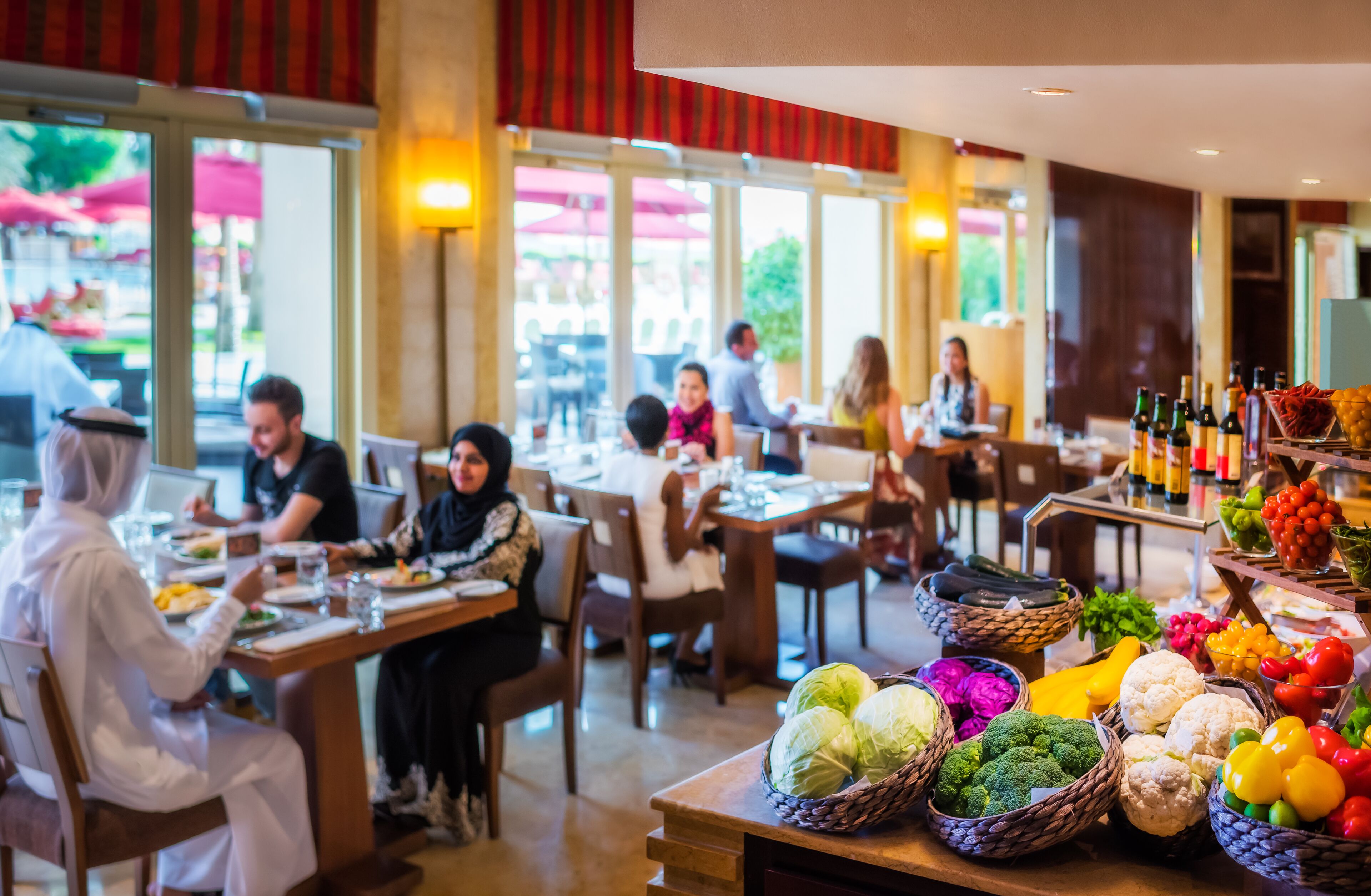 Un restaurant avec des tables et des chaises, un buffet proposant des légumes et des bouteilles de vin disposées sur un comptoir.