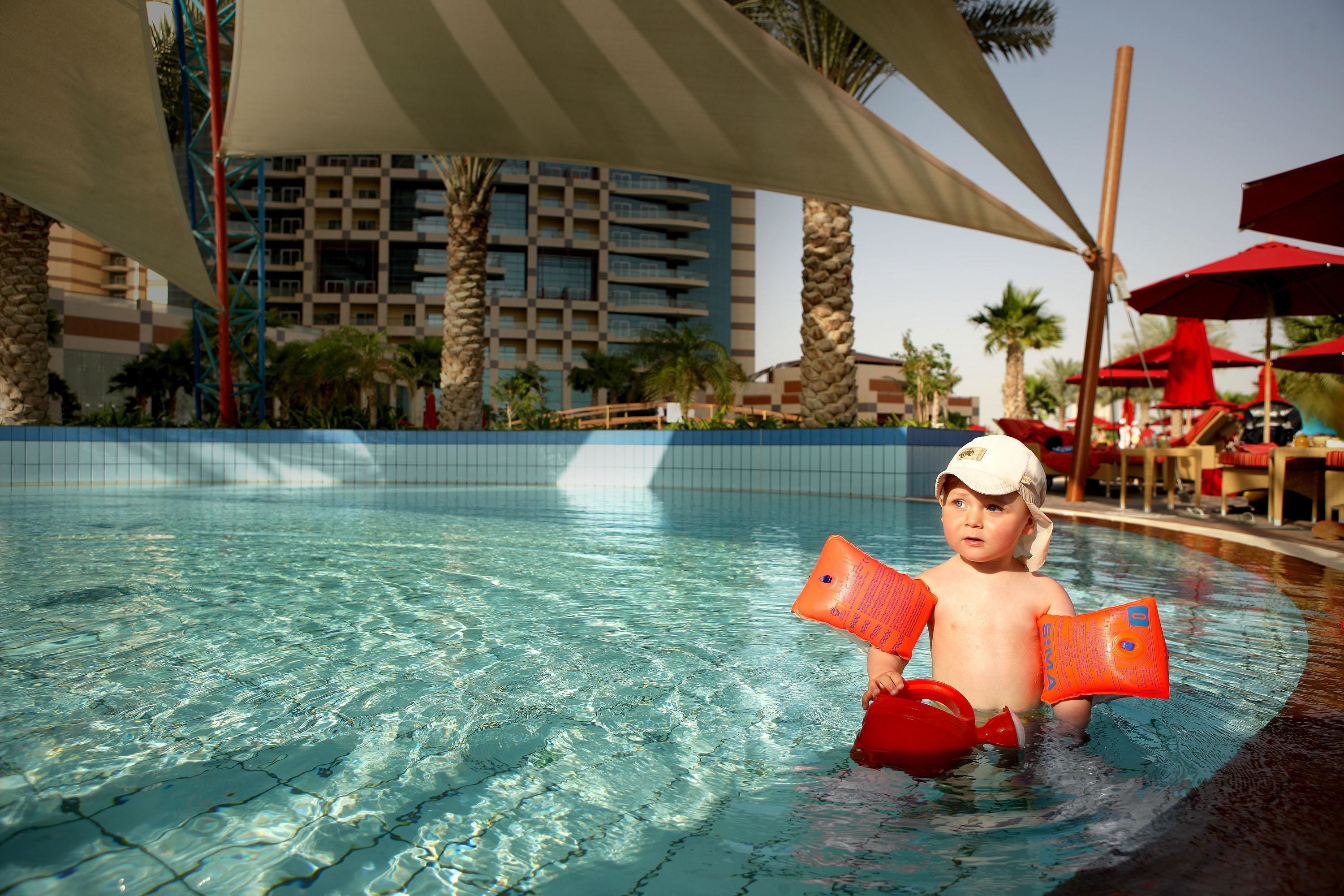 A pool area with clear water, palm trees, and a building in the background.