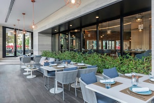 Un área de comedor al aire libre con mobiliario moderno, ventanas amplias y abundante vegetación.